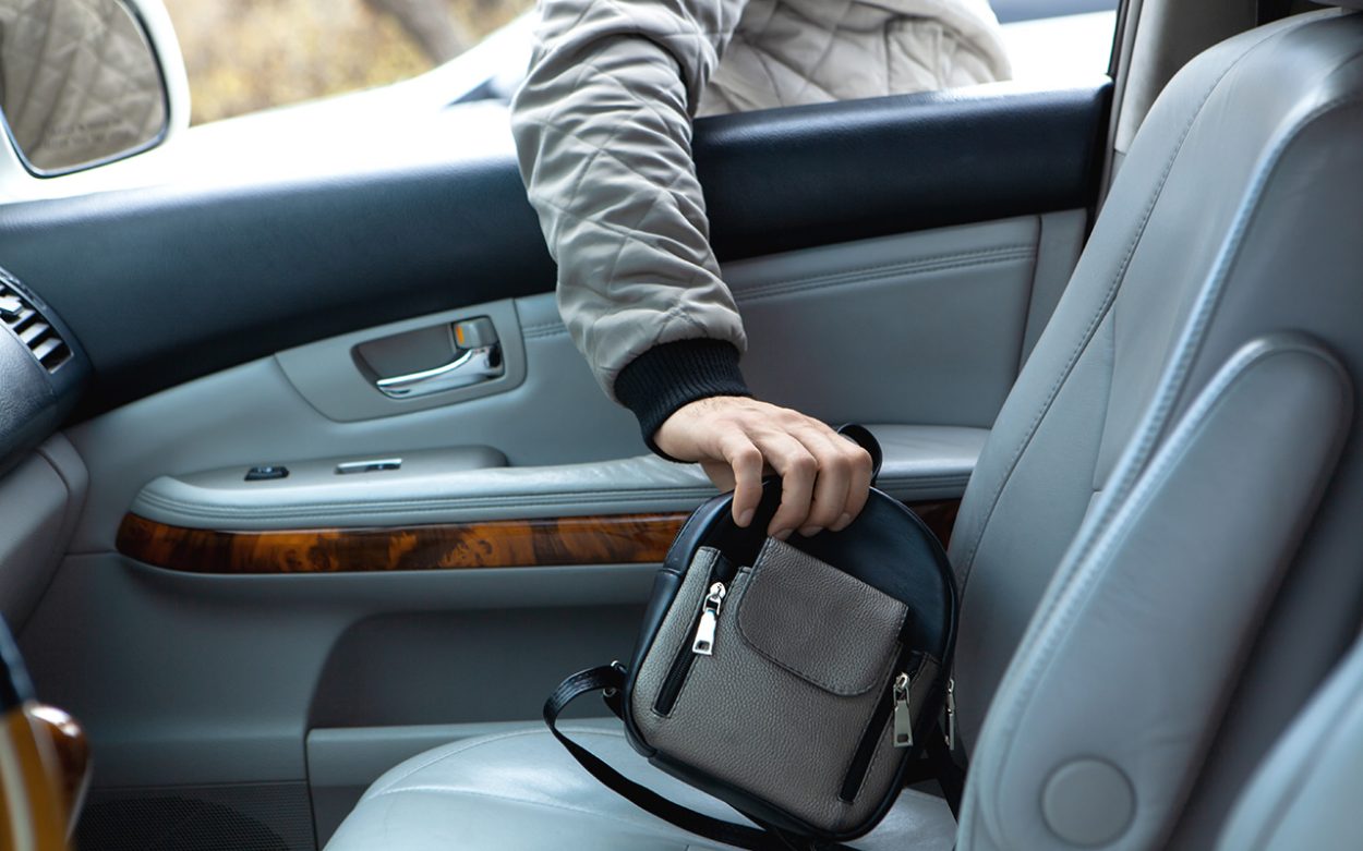 An image of a hand reaching in to a car steal a handbag.