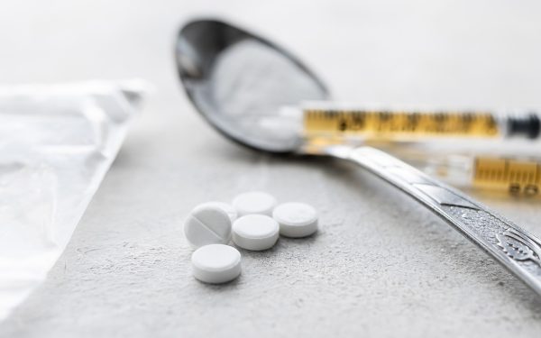 Narcotic substances in a spoon, dope powder in transparent plastic bag, syringes with dose of drugs and white pills on a textured background. Concept of addiction and bad habits